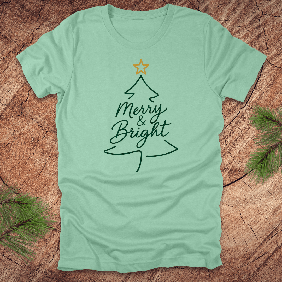 Mint green t-shirt with Christmas tree design and 'Merry & Bright' text on a wooden surface.