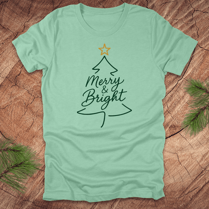 Mint green t-shirt with Christmas tree design and 'Merry & Bright' text on a wooden surface.