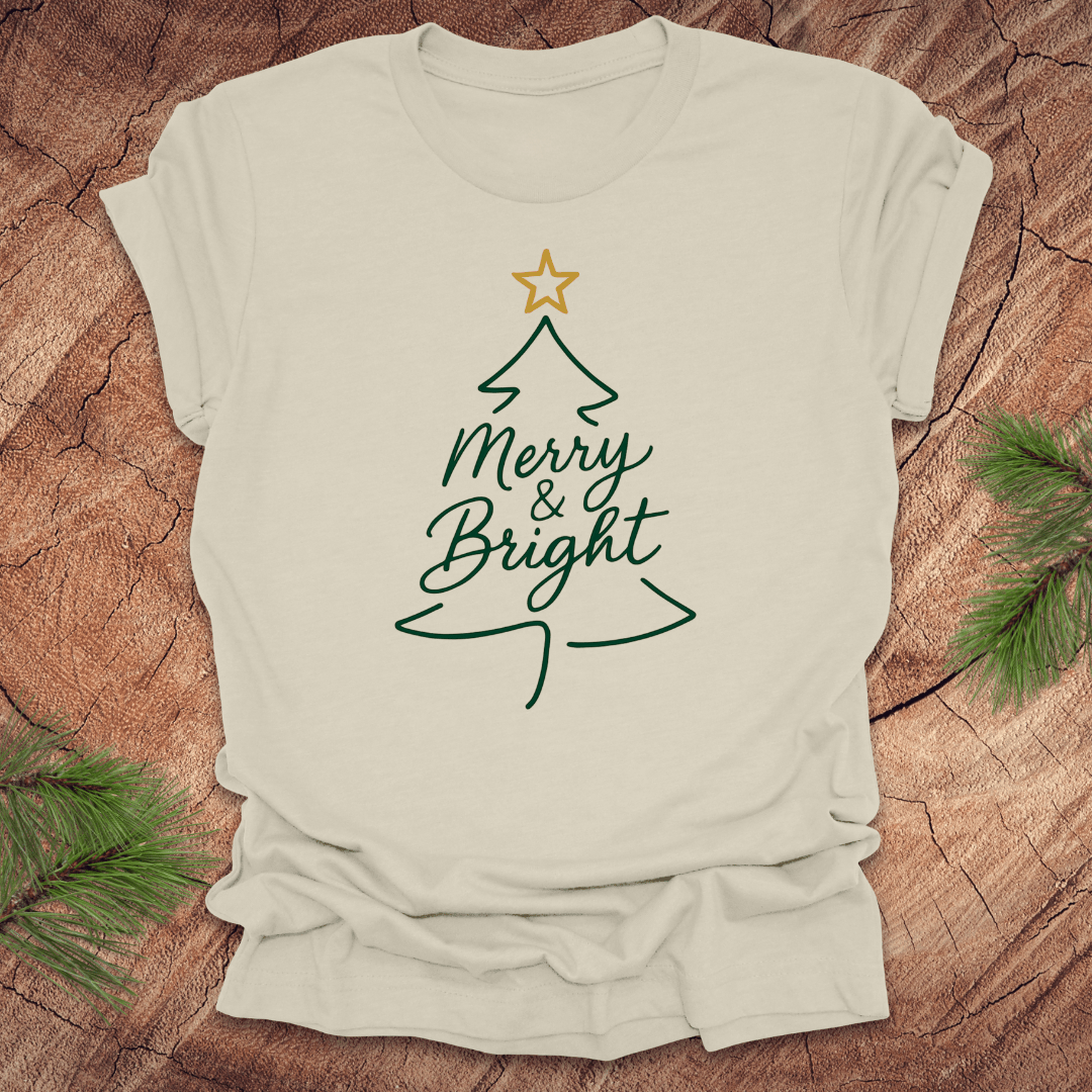 Beige t-shirt with Christmas tree design and 'Merry & Bright' text on a wooden surface.