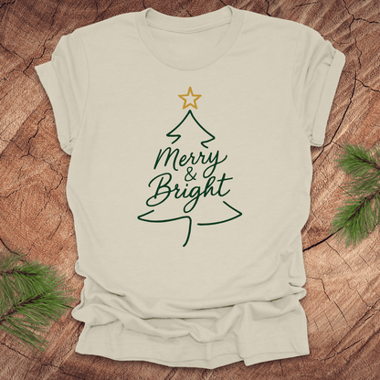 Beige t-shirt with Christmas tree design and 'Merry & Bright' text on a wooden surface.