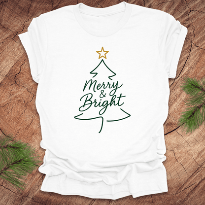 White t-shirt with Christmas tree design and 'Merry & Bright' text on a wooden surface.