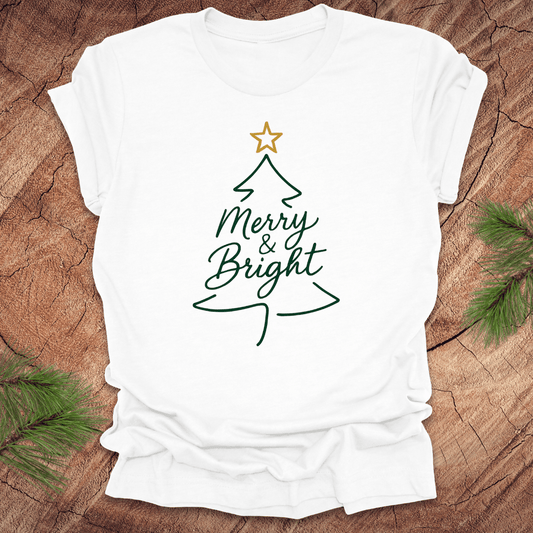White t-shirt with Christmas tree design and 'Merry & Bright' text on a wooden surface.