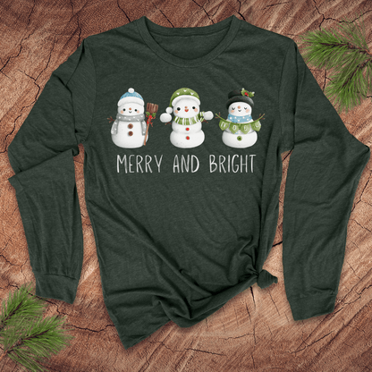 Green long-sleeve shirt with snowman design and 'Merry and Bright' text on a wooden surface.