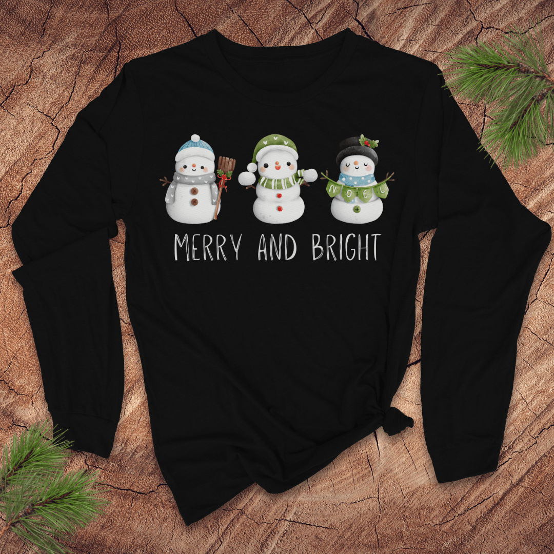 Black long-sleeve shirt with snowman design and 'Merry and Bright' text on a wooden surface.