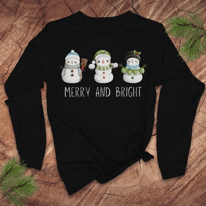 Black long-sleeve shirt with snowman design and 'Merry and Bright' text on a wooden surface.