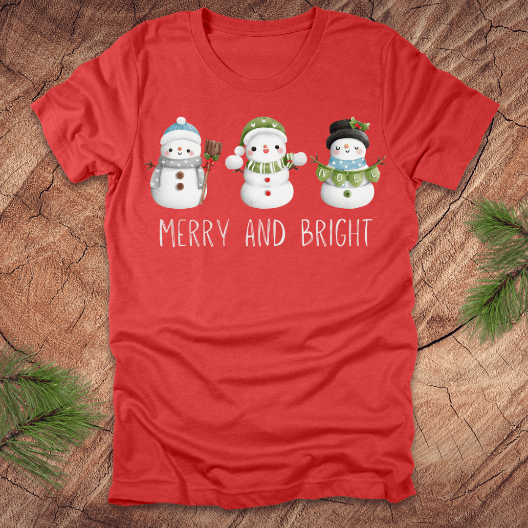 Red t-shirt with snowman design and 'Merry and Bright' text on a wooden surface.