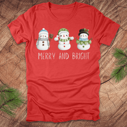 Red t-shirt with snowman design and 'Merry and Bright' text on a wooden surface.