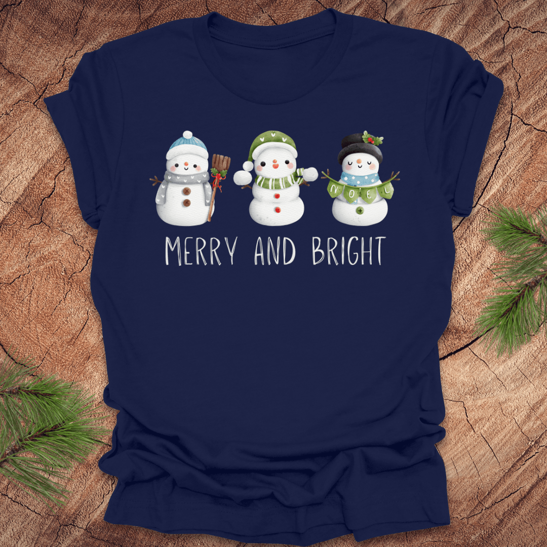 Navy blue t-shirt with snowman design and 'Merry and Bright' text on a wooden surface.