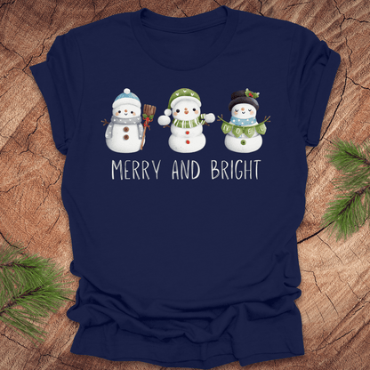 Navy blue t-shirt with snowman design and 'Merry and Bright' text on a wooden surface.