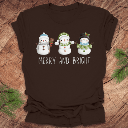 Brown t-shirt with snowman design and 'Merry and Bright' text on a wooden surface.