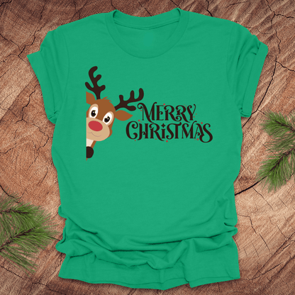 Green t-shirt with a reindeer peeking out from the side and 'Merry Christmas' text on a wooden surface.