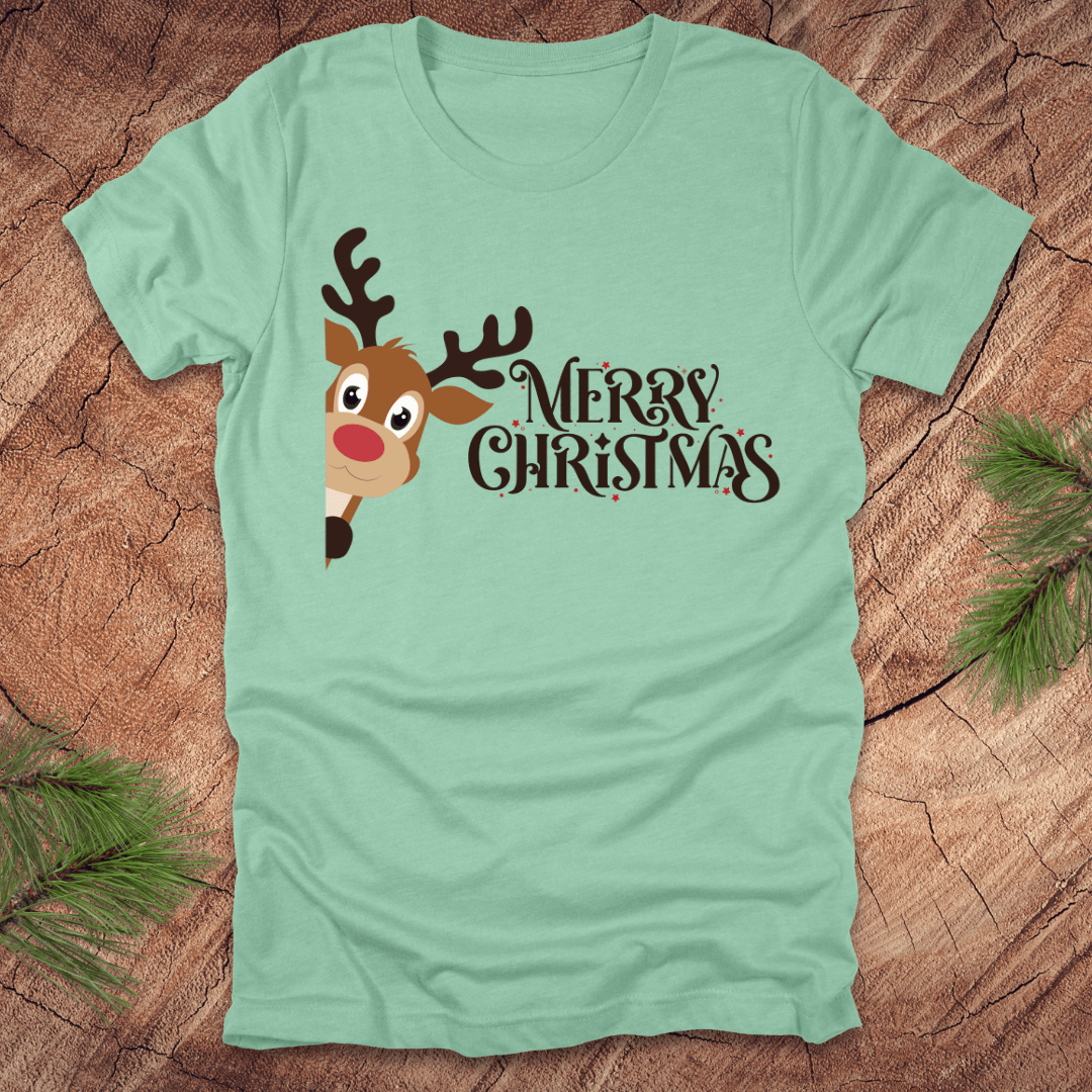 Mint green t-shirt with a reindeer peeking out from the side and 'Merry Christmas' text on a wooden surface.
