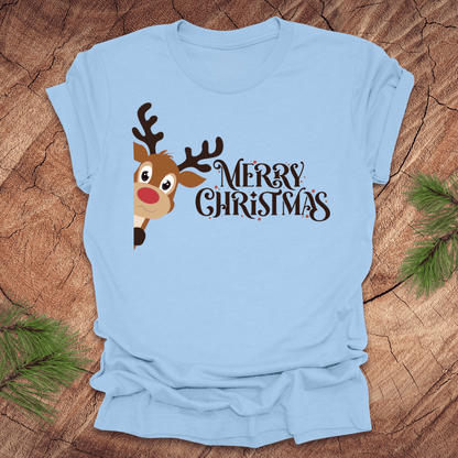 Light blue t-shirt with a reindeer peeking out from the side and 'Merry Christmas' text on a wooden surface.