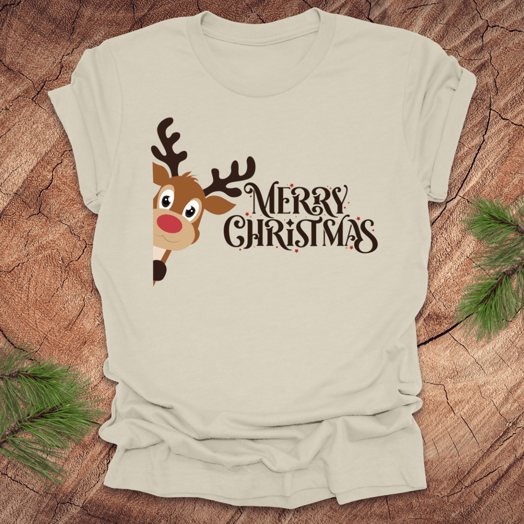 Beige t-shirt with a reindeer peeking out from the side and 'Merry Christmas' text on a wooden surface.