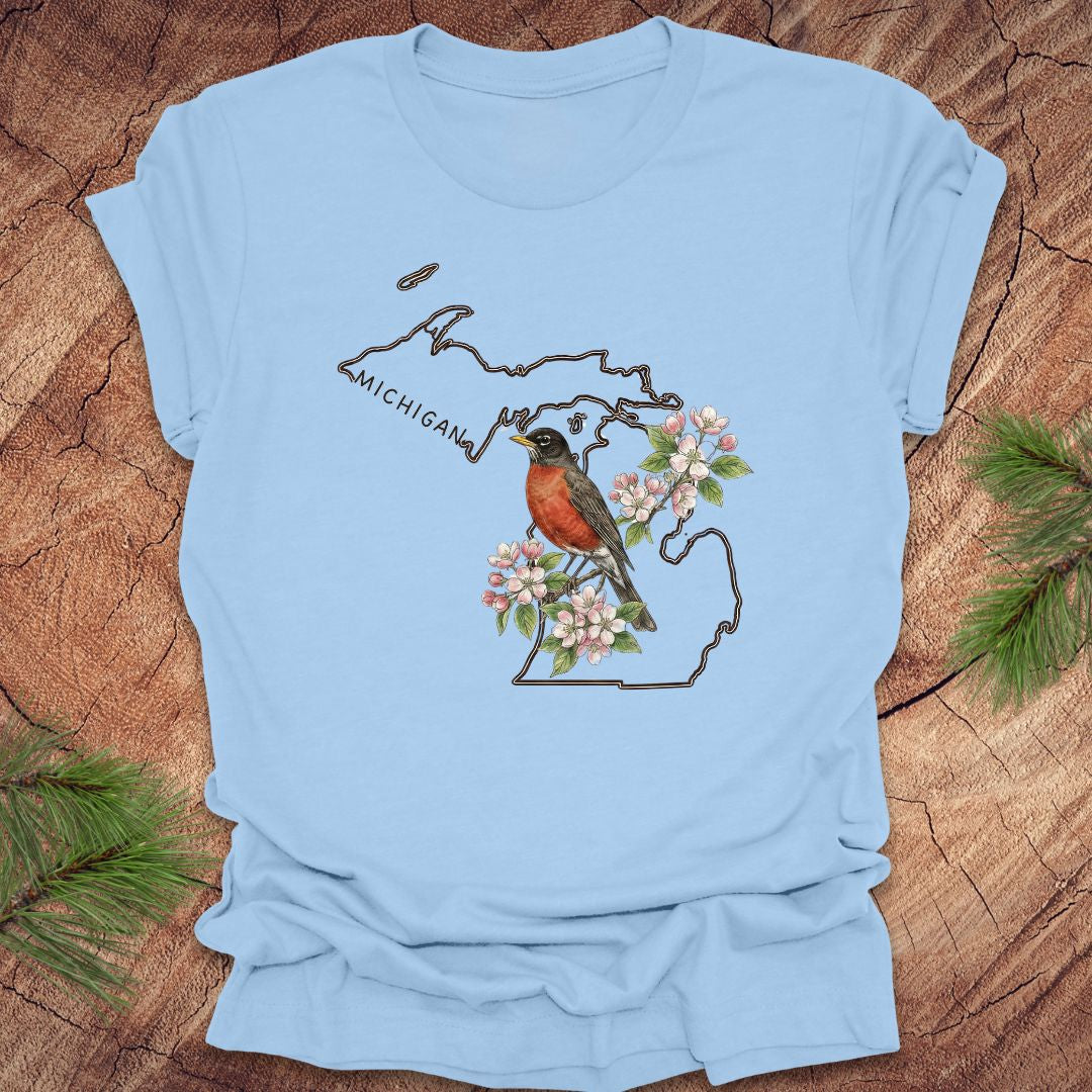 Baby blue t-shirt with Michigan-themed design featuring a robin and apple blossom on a wooden surface.
