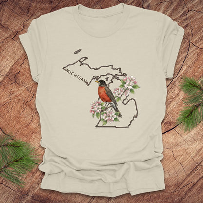 Beige t-shirt with Michigan-themed design featuring a robin and apple blossom on a wooden surface.