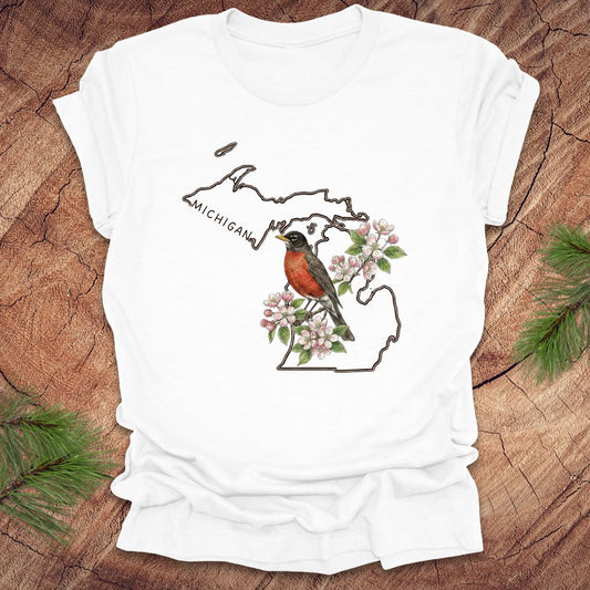 White t-shirt with Michigan-themed design featuring a robin and apple blossom on a wooden surface.