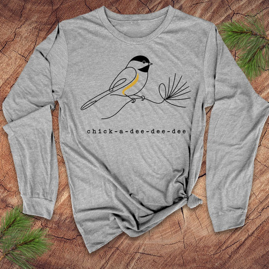 Gray long-sleeve shirt with chickadee design and 'chick-a-dee-dee-dee' text on a wooden surface.