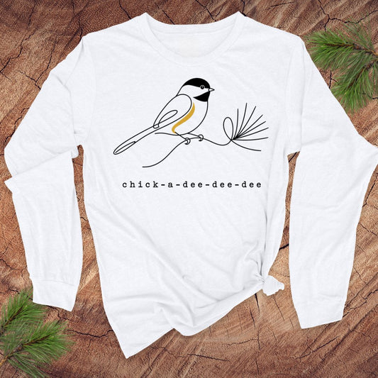 White long-sleeve shirt with chickadee design and 'chick-a-dee-dee-dee' text on a wooden surface.