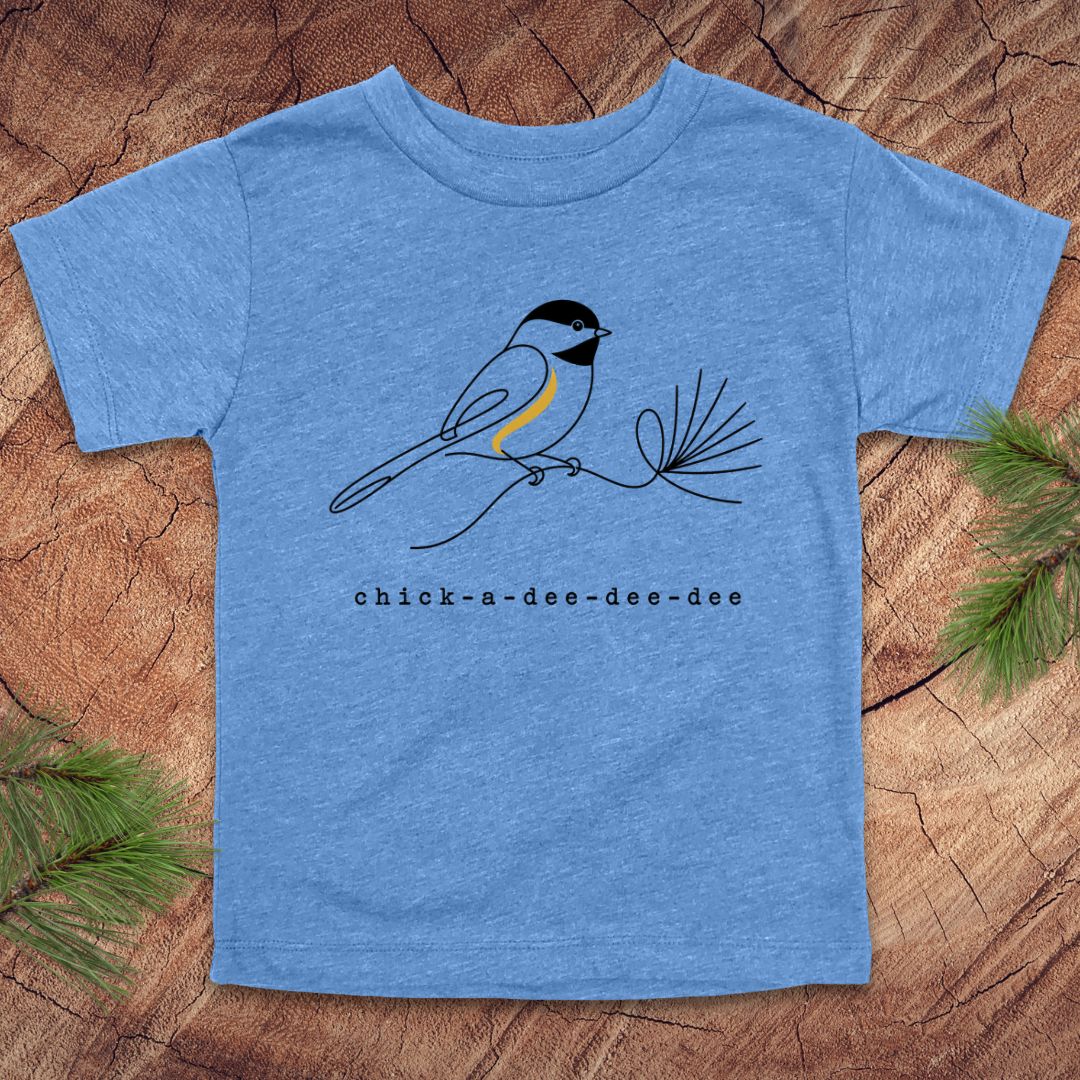 A kids' heather blue short-sleeve t-shirt featuring a black and white chickadee bird with a yellow chest, perched on a pine branch. Below the bird is the text 'chick-a-dee-dee-dee'.