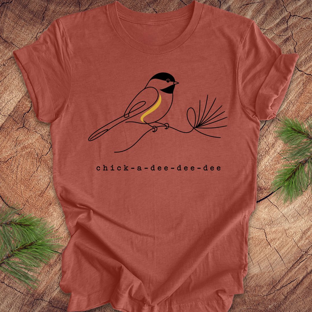 Red t-shirt with a chickadee design and 'chick-a-dee-dee-dee' text on a wooden surface.