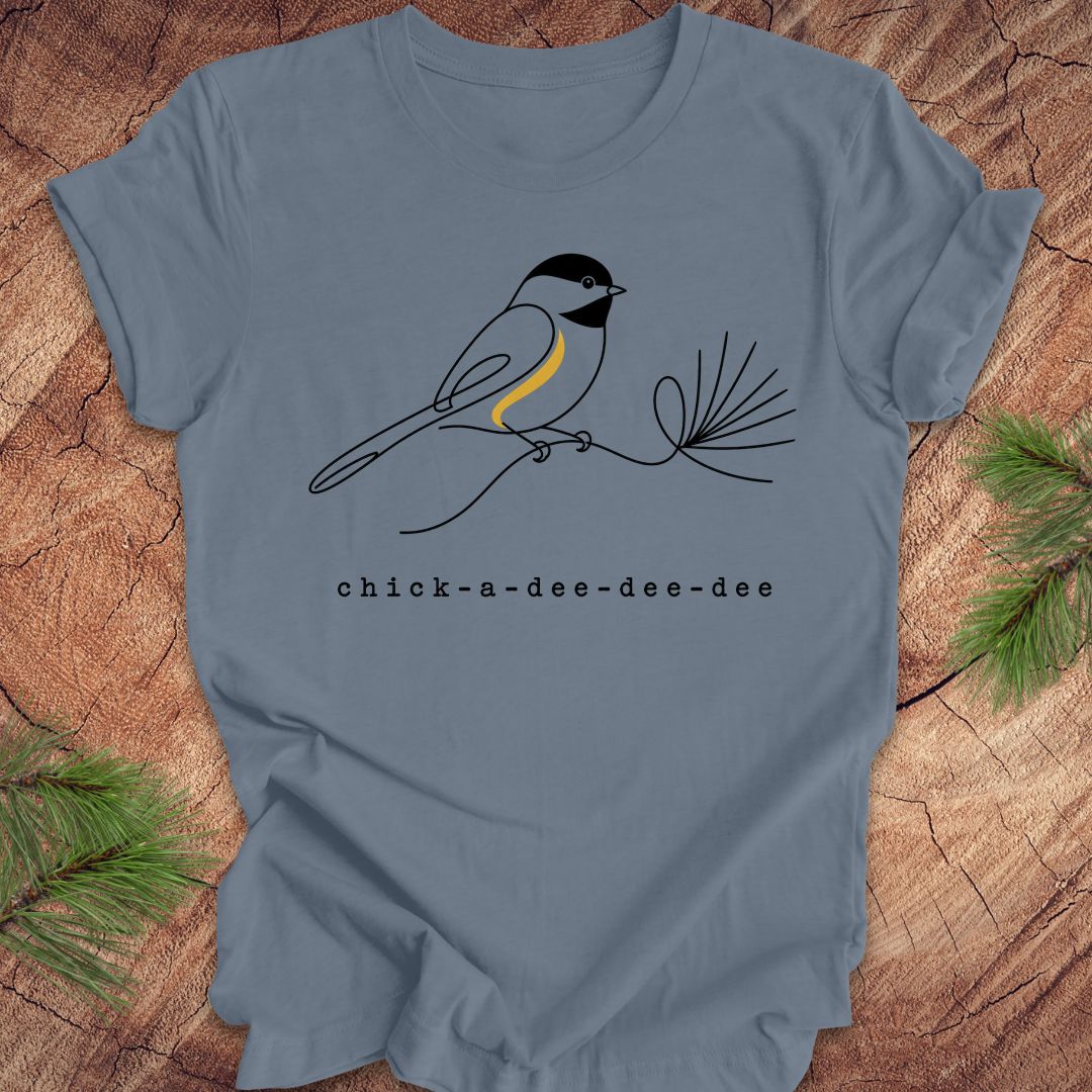 Blue t-shirt with a chickadee design and 'chick-a-dee-dee-dee' text on a wooden surface.