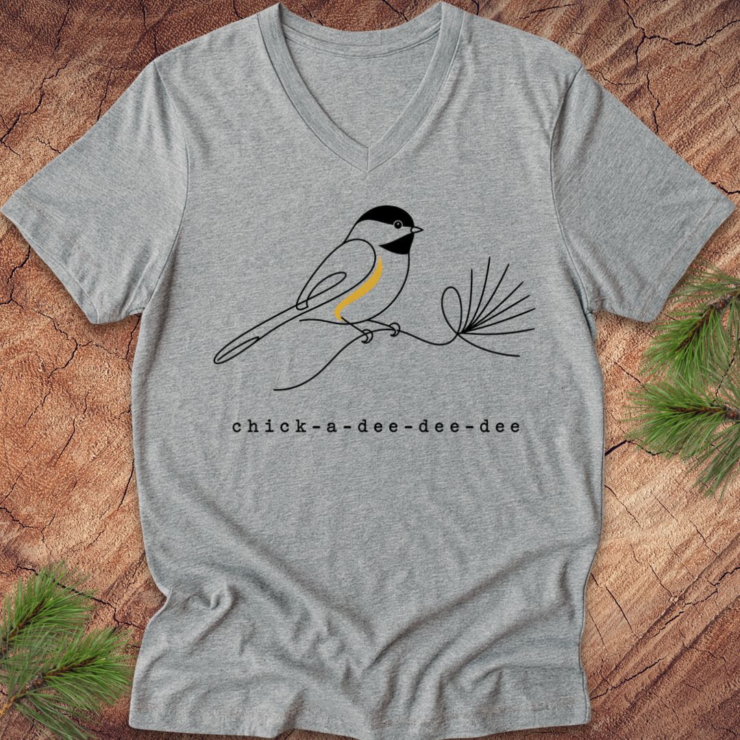 Gray t-shirt with a chickadee design and 'chick-a-dee-dee-dee' text on a wooden surface.