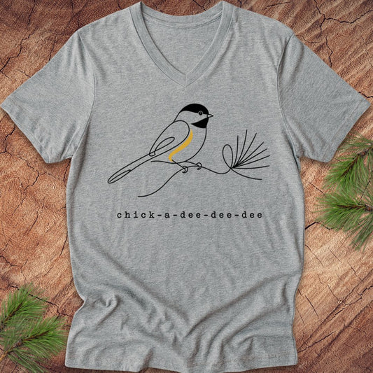 Gray t-shirt with a chickadee design and 'chick-a-dee-dee-dee' text on a wooden surface.