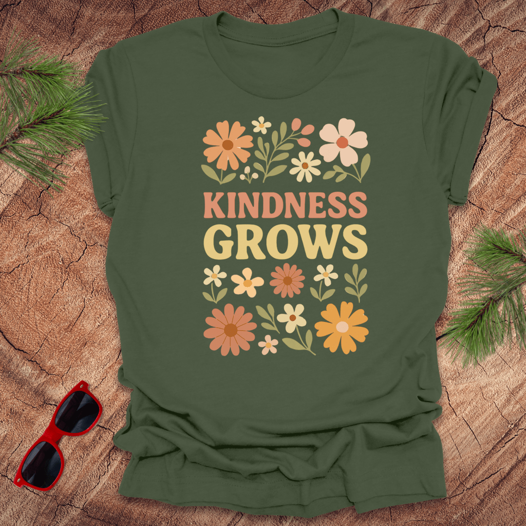 Green t-shirt with flowers and text 'Kindness Grows' on a wood background.