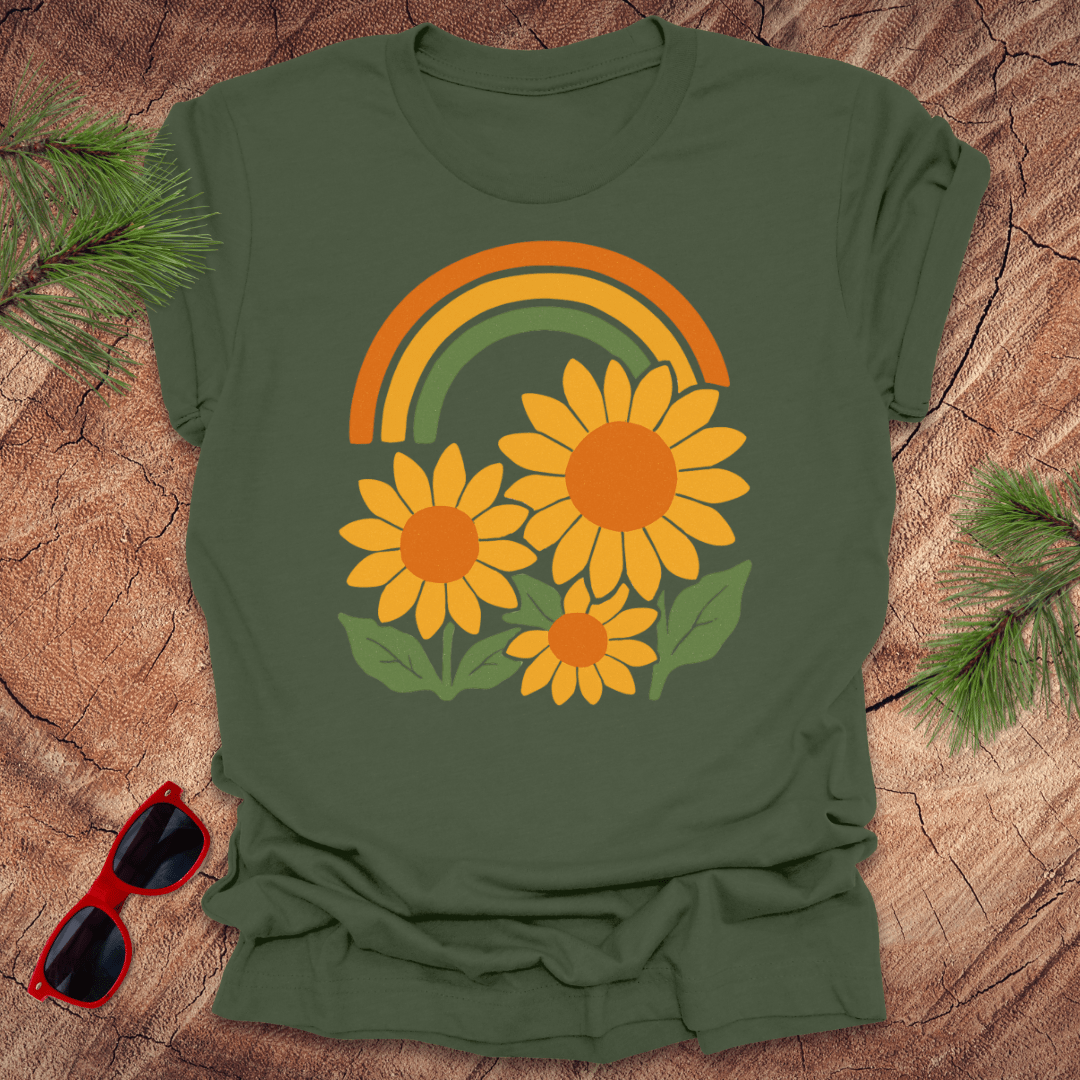 Green t-shirt with a rainbow and sunflower design on a wooden surface with sunglasses.
