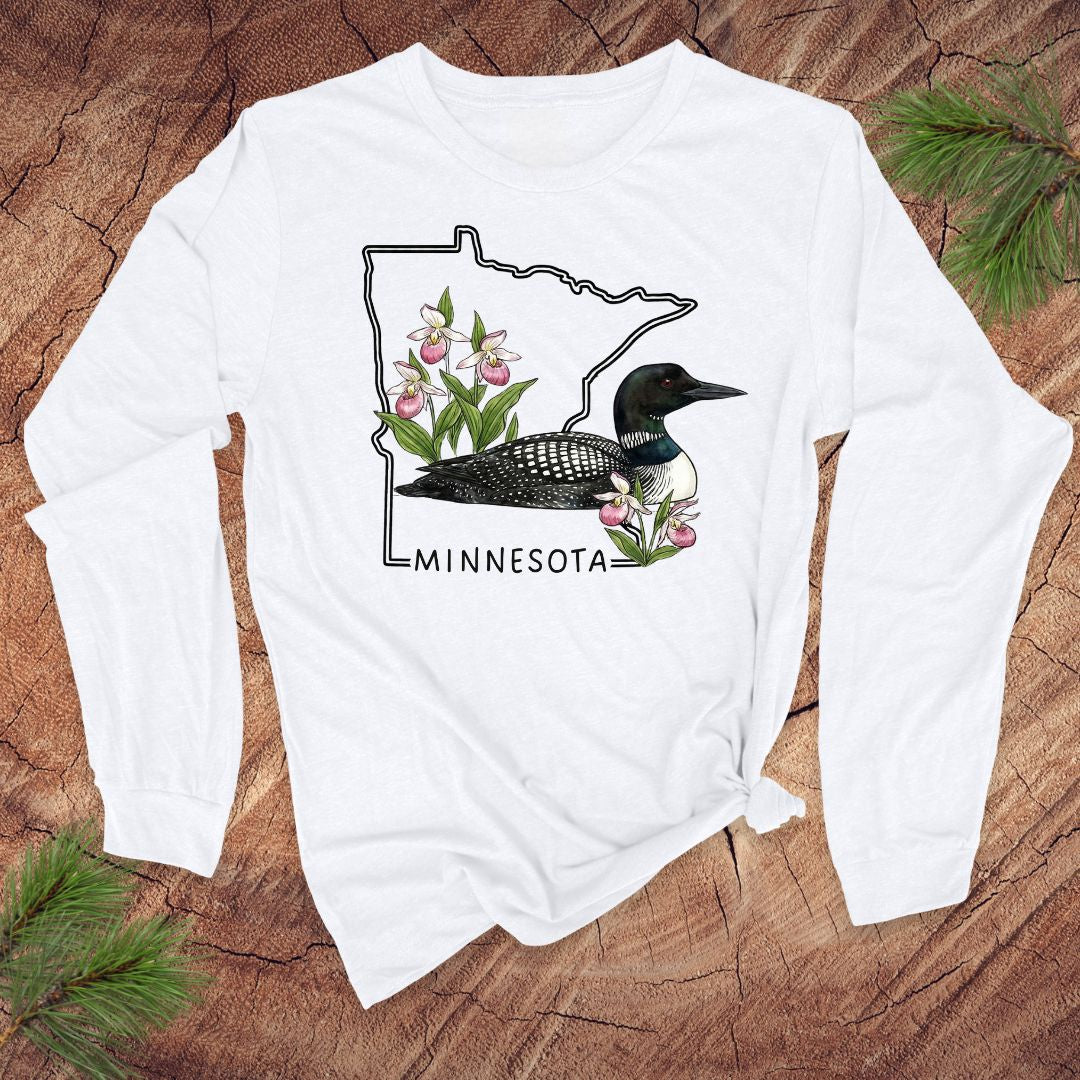 White long-sleeve shirt with Minnesota loon and flower design on a wooden surface