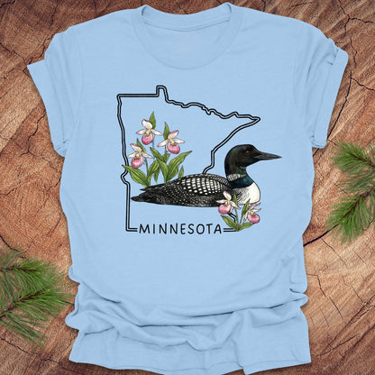 Baby blue t-shirt with Minnesota state outline and loon design on a wooden surface