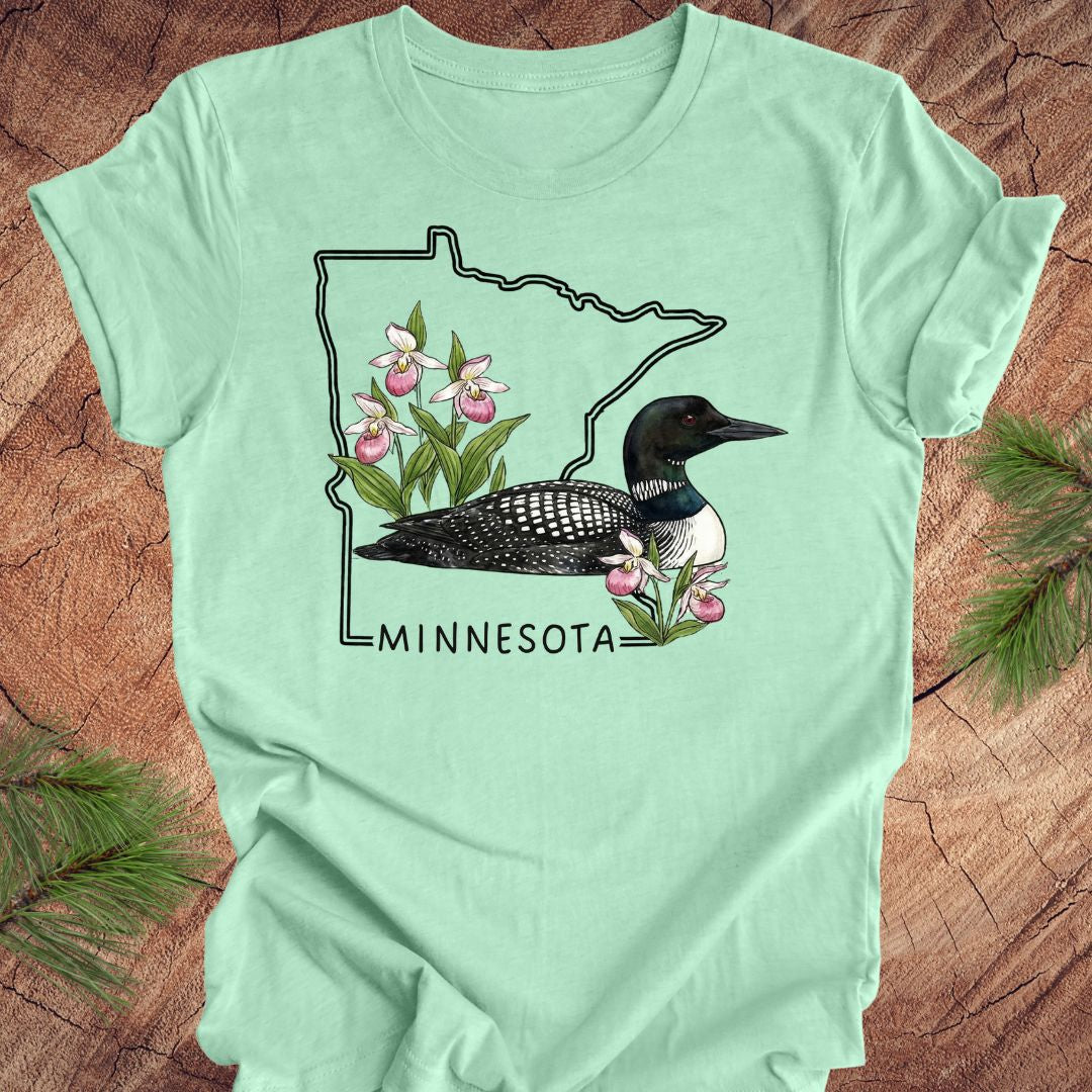 Mint green t-shirt with Minnesota loon and orchid design on a wooden surface
