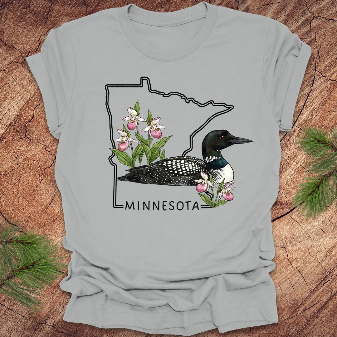 Silver t-shirt with Minnesota state outline and loon design on a wooden surface