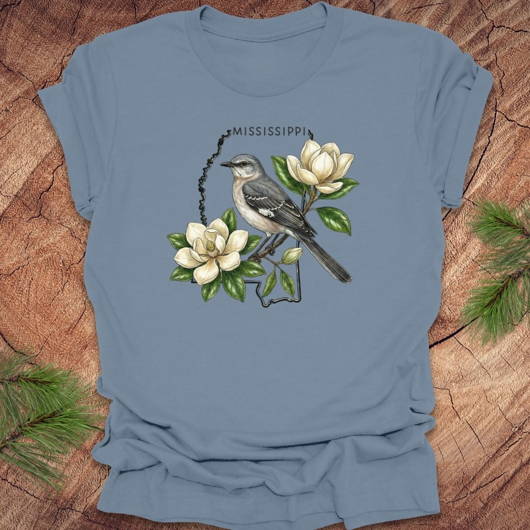 Steel blue t-shirt with the outline of Mississippi with state bird, mockingbird and flower, magnolia, on a wooden surface
