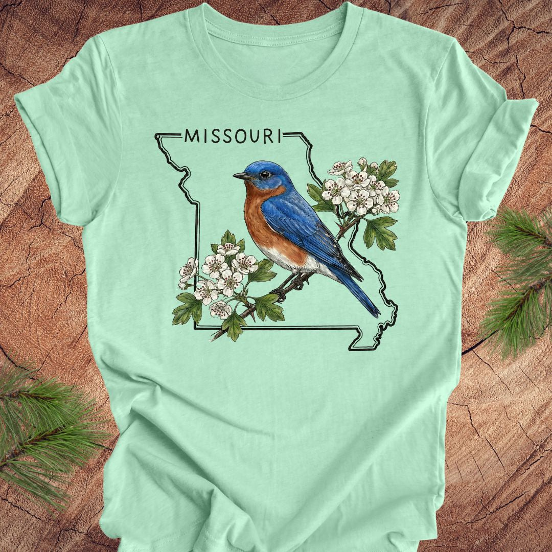 Light green t-shirt with a bluebird and Missouri outline design on a wooden surface.