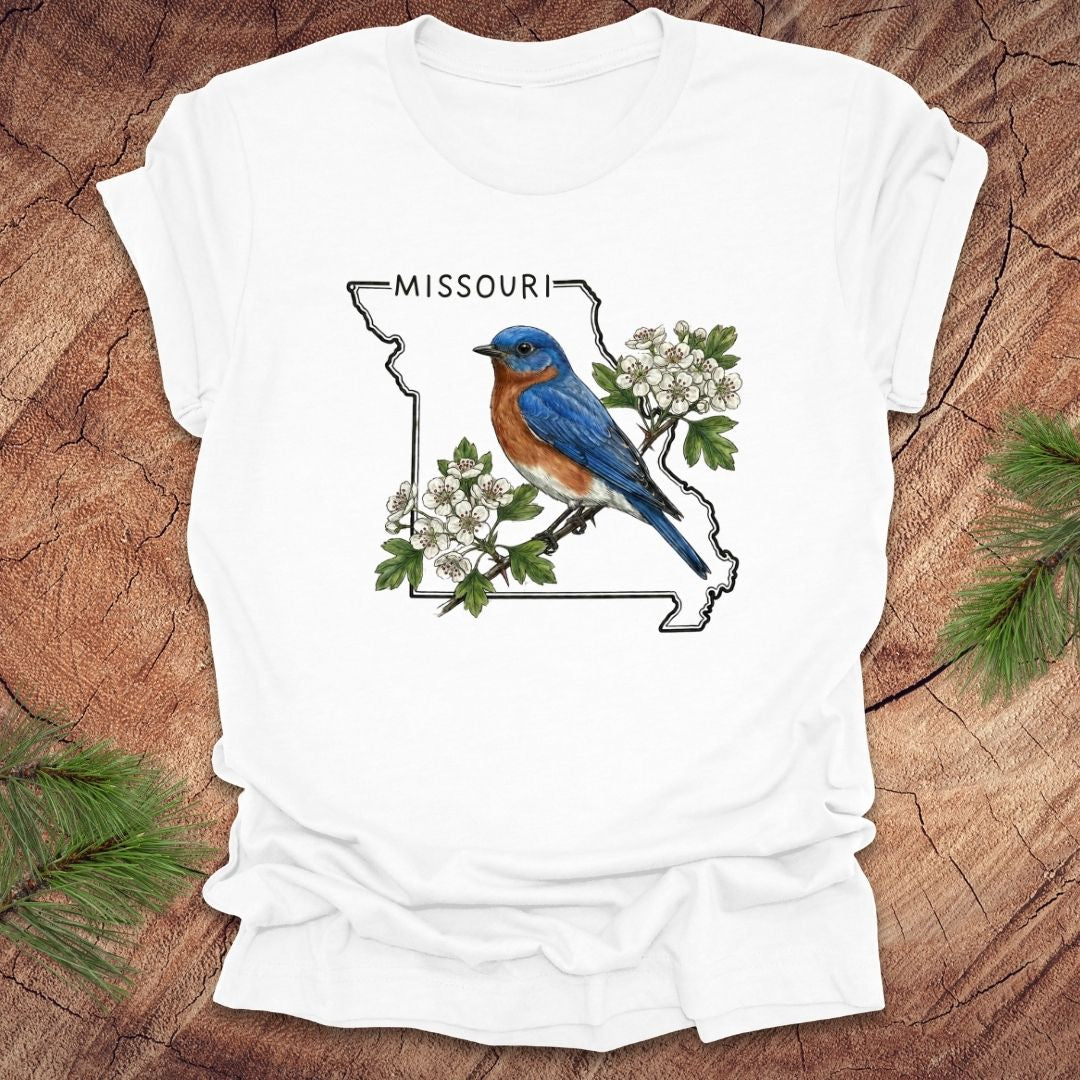White t-shirt with a bluebird and Missouri state outline design on a wooden surface.