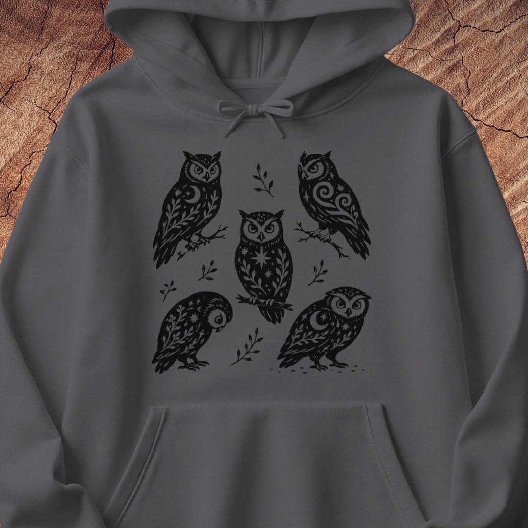 Charcoal gray hoodie with black folk-art owls decorated with crescent moons, stars, and vines, laid flat on a rustic wood background.