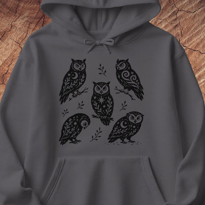 Charcoal gray hoodie with black folk-art owls decorated with crescent moons, stars, and vines, laid flat on a rustic wood background.