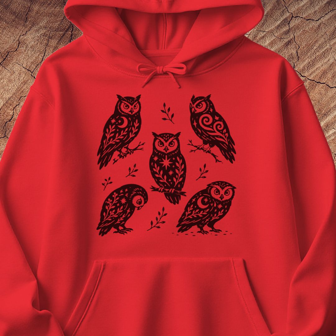 Red hoodie with black folk-art owls decorated with crescent moons, stars, and vines, laid flat on a rustic wood background.