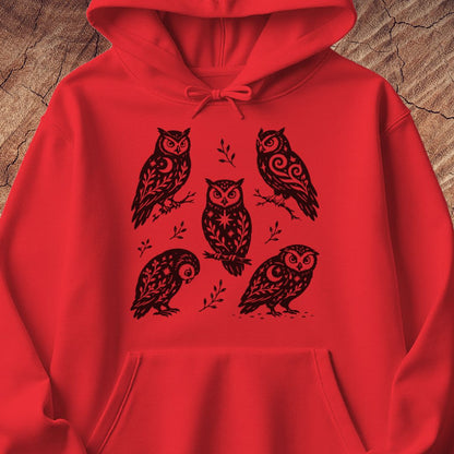 Red hoodie with black folk-art owls decorated with crescent moons, stars, and vines, laid flat on a rustic wood background.