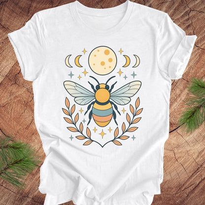 White t-shirt with a bee and moon design on a wooden surface