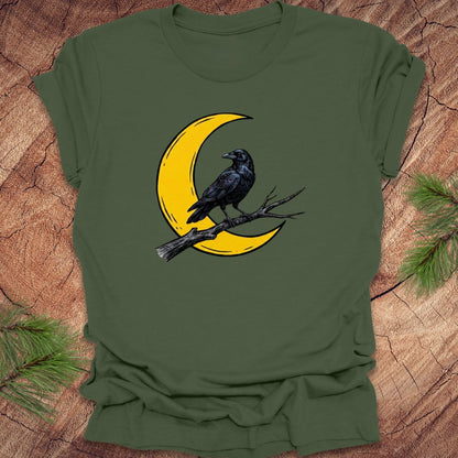 Green t-shirt with a yellow crescent moon and black crow design on a wooden surface.
