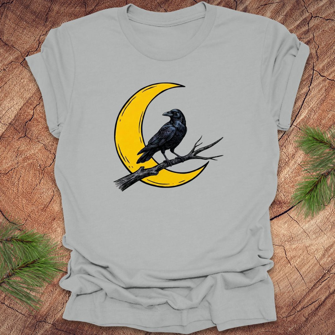 Gray t-shirt with a yellow crescent moon and black crow design on a wooden surface.