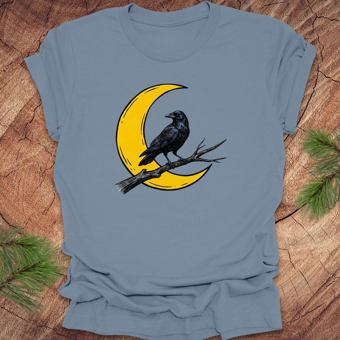 Blue t-shirt with a yellow crescent moon and black crow design on a wooden surface.