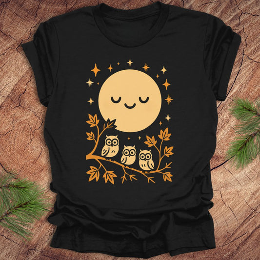 Black t-shirt with a yellow moon and owl design on a wooden surface.