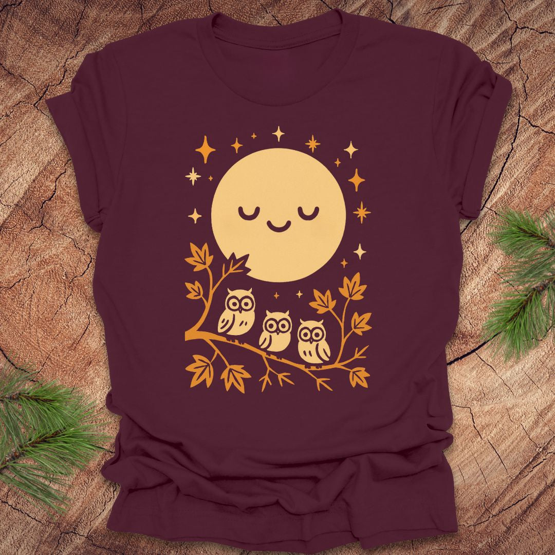 Maroon t-shirt with a yellow moon and owl design on a wooden surface.