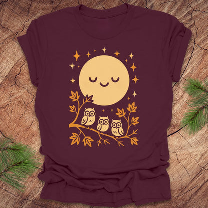 Maroon t-shirt with a yellow moon and owl design on a wooden surface.