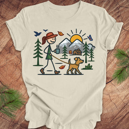 Beige t-shirt with a graphic of a person walking a dog in a forest on a wooden surface.