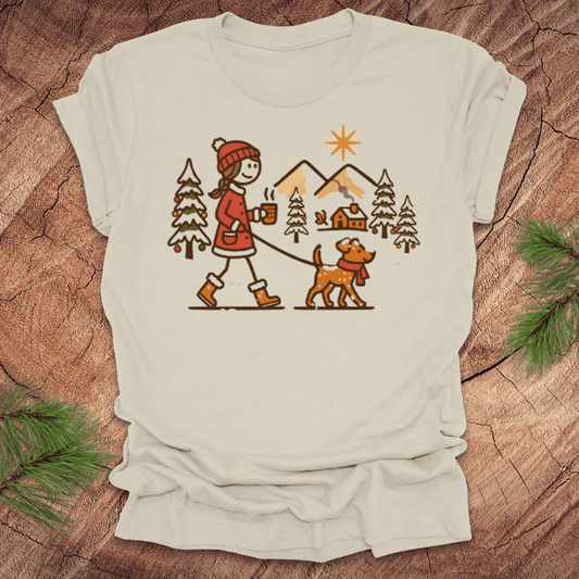 Beige t-shirt with a graphic of a person walking a dog in a winter scene on a wooden surface.